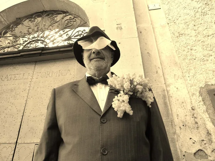 Ritratto di un figurante del Carnevale di Cirigliano, in giacca, cravatta a farfalla e cappello, con un fiore all’occhiello
