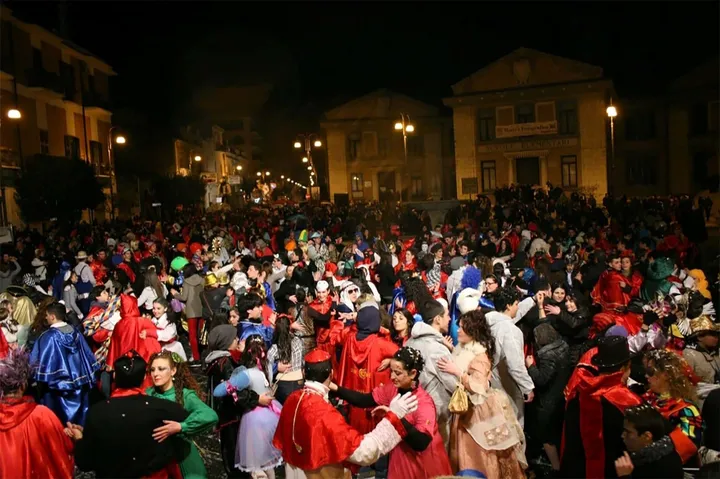 Una piazza gremita di notte durante il Carnevale di Lavello, con le mantelle rosse dei Domini fra la folla