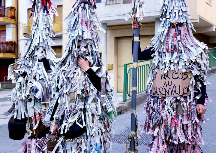 Una maschera del Carnevalone interamente ricoperta di strisce di carta di giornale, in piedi lungo la strada
